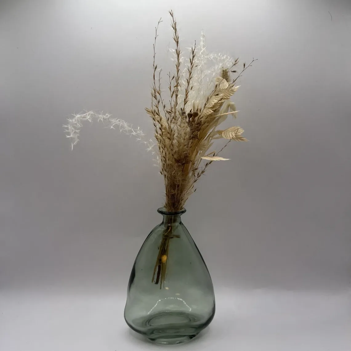 Vase en verre vert élégant avec arrangement floral séché